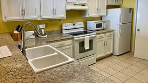 A kitchen with white cabinets, a granite countertop, a sink, a stove, a microwave, and a refrigerator. - Right Price in Paradise! Luxury Ocean Front (South Padre Island)