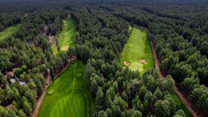 Vista aérea de um campo de golfe rodeado por floresta densa, com vários fairways e bunkers de areia.