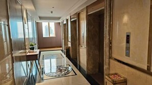 Moderni hotellikäytävä, jossa on lasihissi, pieni pöytä, jossa on kasvi, ja kuvioitu lattia.