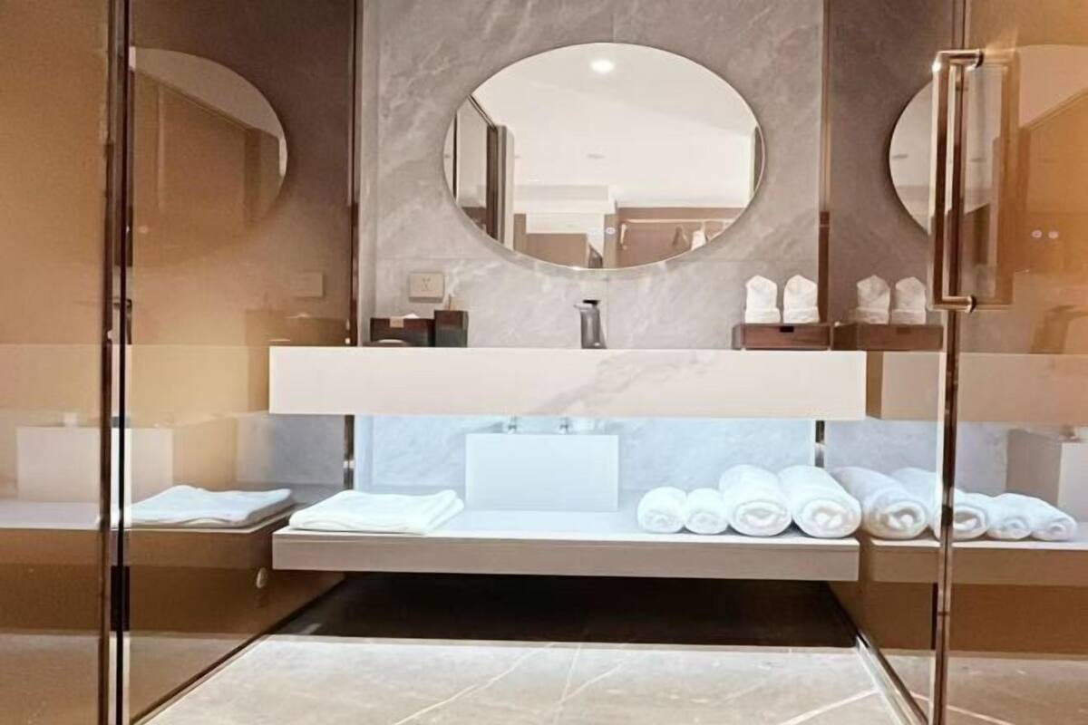 Une salle de bain moderne avec une douche à parois de verre, un meuble-lavabo en marbre et des serviettes soigneusement pliées.