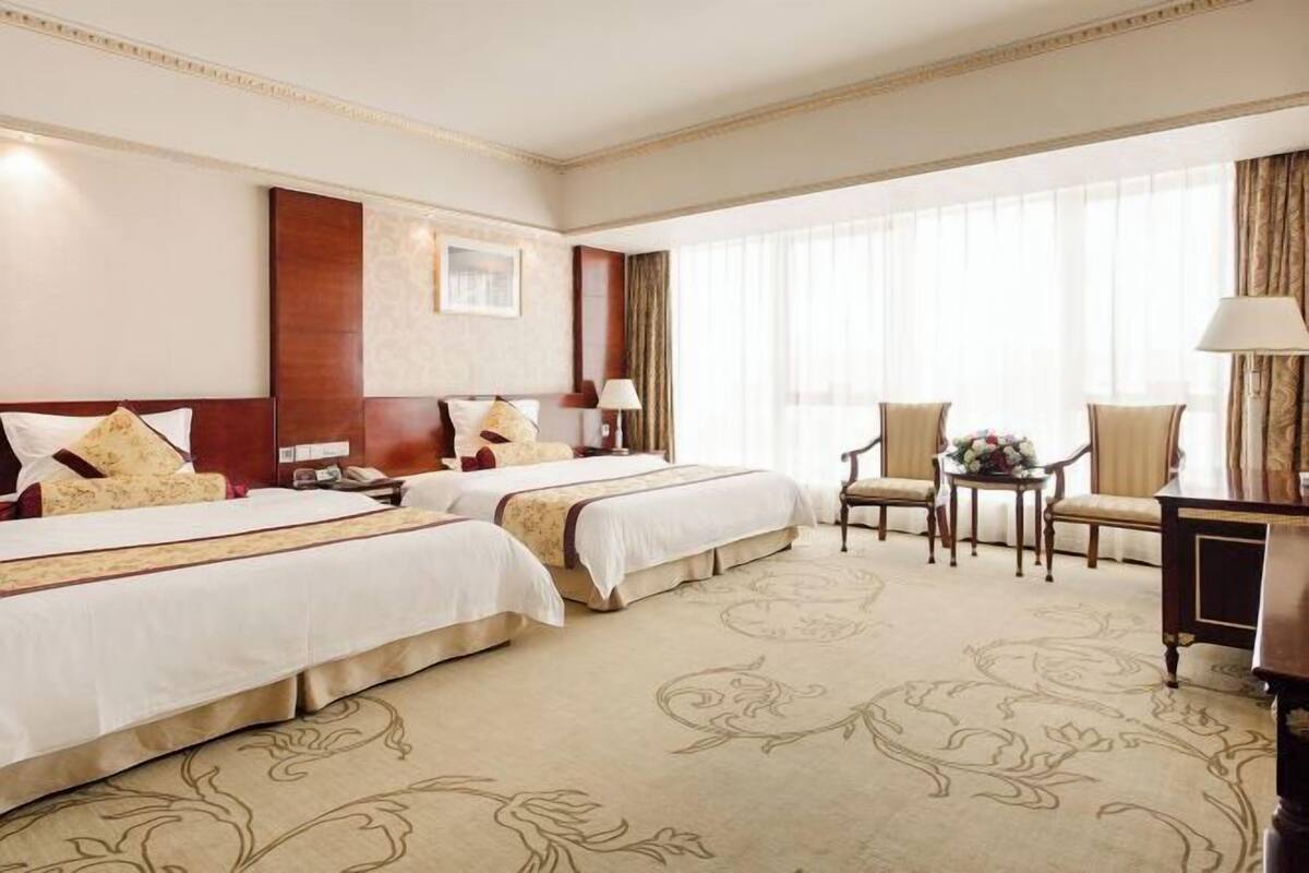 Une chambre d’hôtel avec deux lits, un bureau, une chaise et une grande fenêtre avec des rideaux.