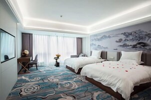 A hotel room with two beds, a desk, a chair, and a large window with curtains.
