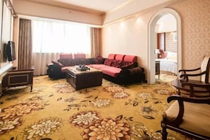 A hotel room with a sofa set, a coffee table, a TV, and a patterned carpet. - Dragon City International Hotel (Heyuan)