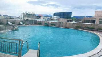 Una piscina de borde curvo, rodeada por un muro bajo y una barandilla metálica.