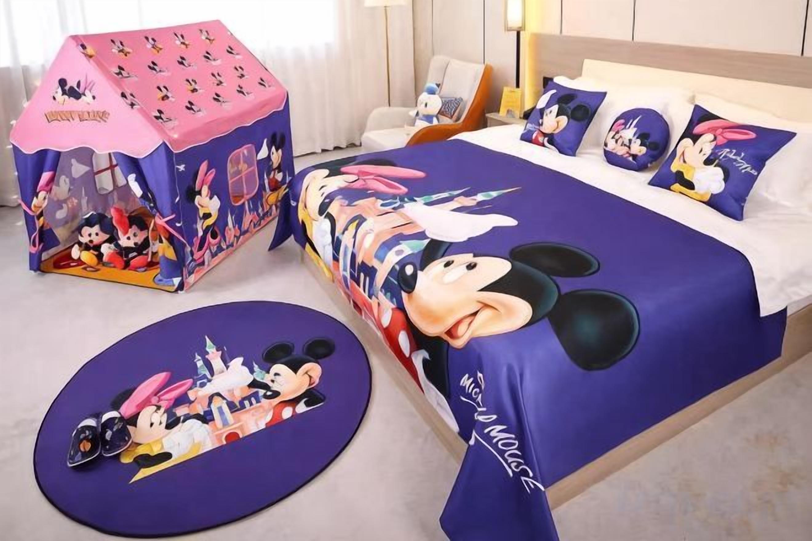 A hotel room with a Mickey Mouse themed bedspread, pillows, and a Mickey Mouse play tent.