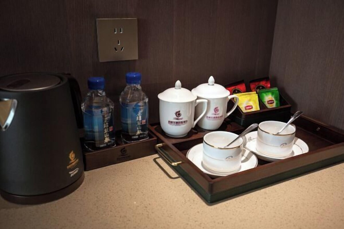 A hotel room's breakfast setup with a coffee maker, water bottles, tea pots, cups, and a tray.