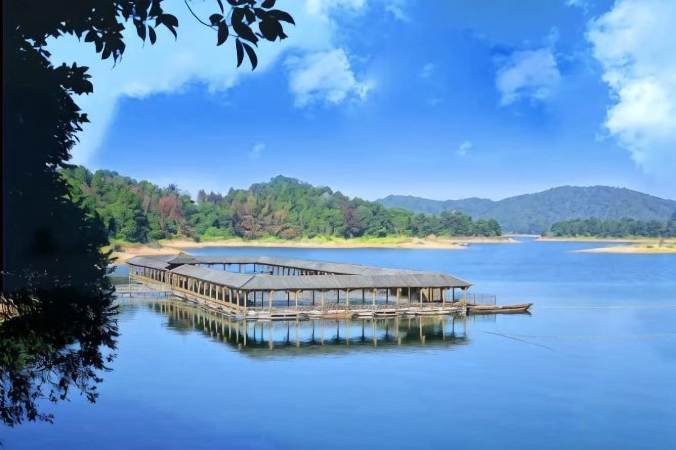 A wooden pier extending into calm water, surrounded by forested hills.