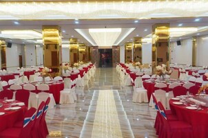 Un salón de banquetes con filas de mesas, cada una con mantel blanco y sillas rojas, y un pasillo central.