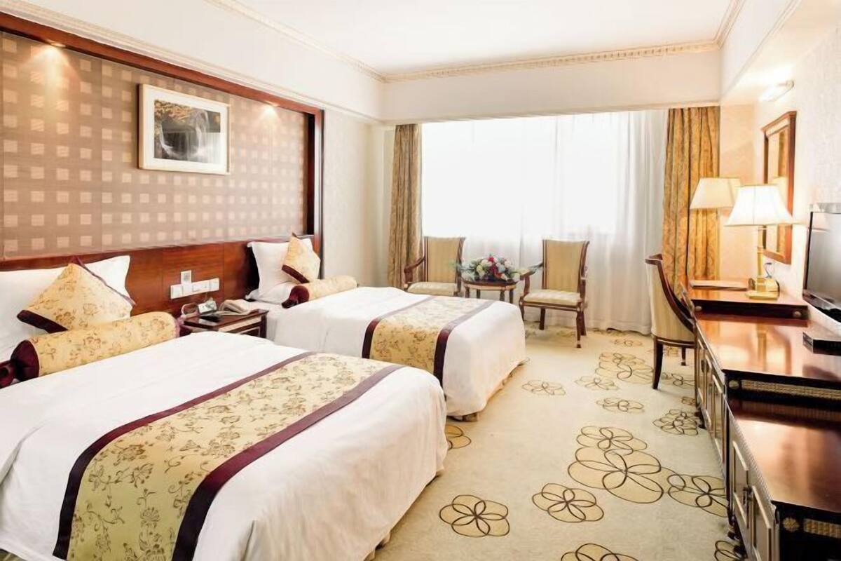 Une chambre d’hôtel avec deux lits, un bureau, une chaise, une télévision et une grande fenêtre avec des rideaux.