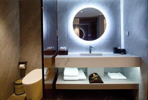 A modern bathroom with a round mirror, a sink, and neatly folded towels on a shelf.