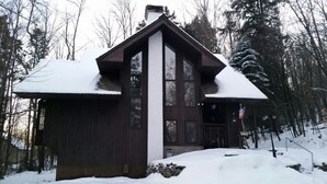 Eine Holzhütte mit steilem Dach, großen Fenstern und einem Steinfundament.