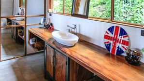 Ein modernes Badezimmer mit Waschtisch aus Holz, einem großen Fenster mit Blick ins Grüne und einem Spiegel, der den Raum widerspiegelt.