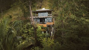 Ein zweistöckiges Holzhaus, umgeben von üppiger tropischer Vegetation.