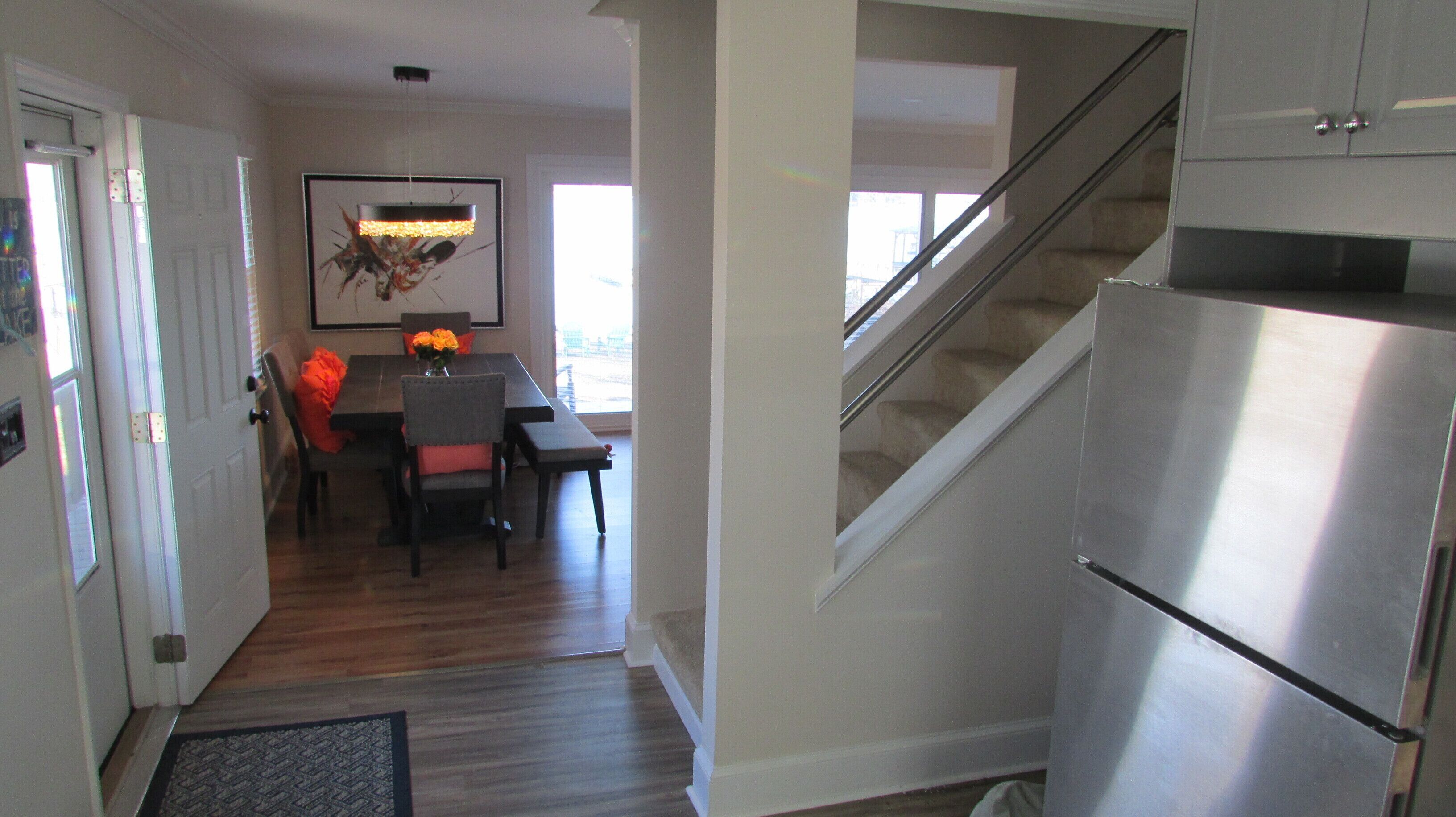 A modern kitchen with a stainless steel refrigerator, wooden flooring, and a dining area with a table and chairs.