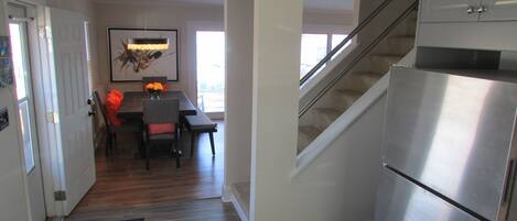 A modern kitchen with a stainless steel refrigerator, wooden flooring, and a dining area with a table and chairs.