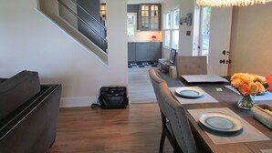 Une cuisine moderne avec des meubles gris, un coin repas avec une table en bois dressée pour deux personnes, et un escalier menant à l’étage supérieur.