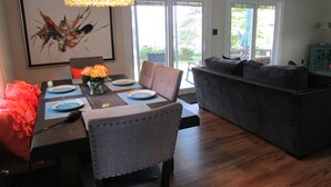 Un coin repas avec une table dressée pour quatre personnes, un canapé gris recouvert de tissu et un lustre.