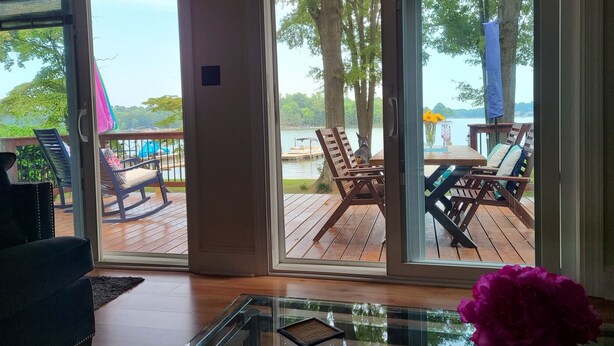 Une pièce avec une table en verre, un canapé sombre et une vue sur une terrasse extérieure dotée de chaises et d’une table en bois.