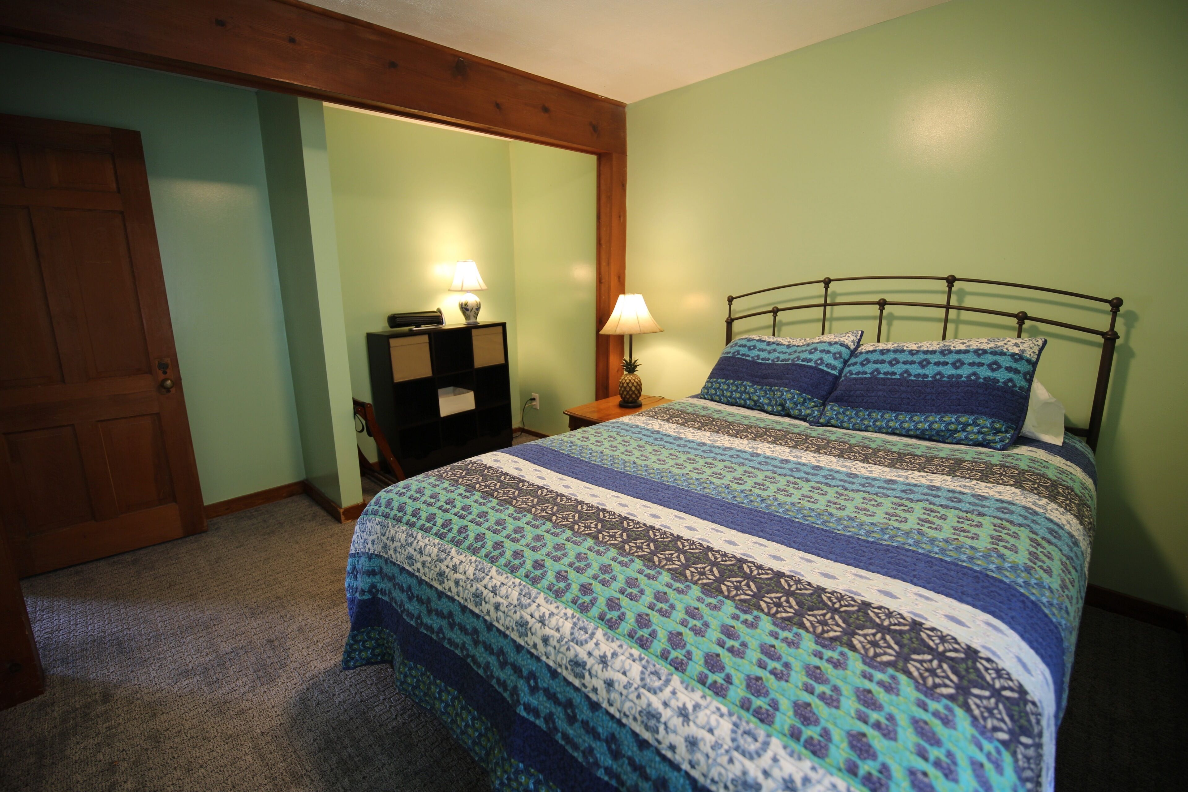 A bedroom with a bed, a nightstand, a lamp, and a wooden door.