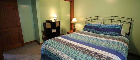 A bedroom with a bed, a nightstand, a lamp, and a wooden door.