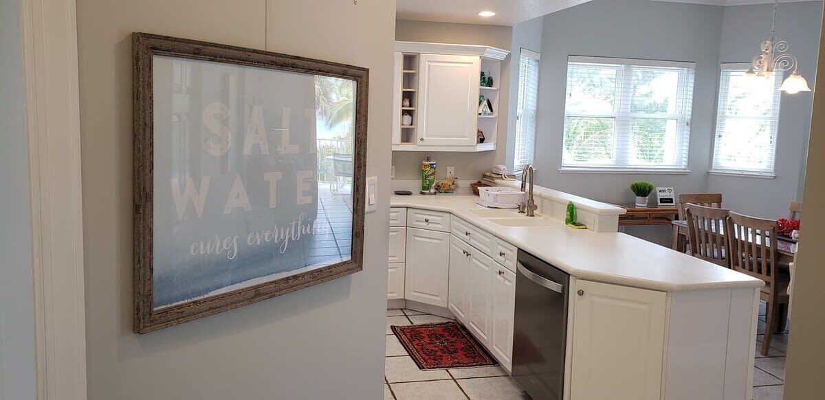 A kitchen with white cabinets, a red rug, and a framed sign on the wall.