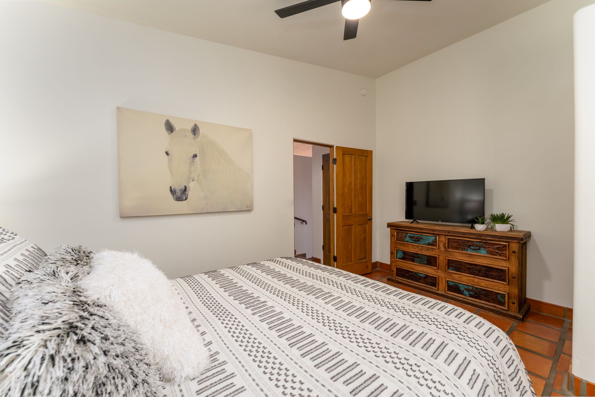 Een slaapkamer met een bed, een televisie, een houten dressoir en een schilderij aan de muur.