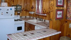A compact kitchen with wooden walls, a white refrigerator, a stove, and a tiled countertop.
