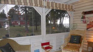 A cozy room with wicker chairs, a red folding chair, and a view of a house and trees through large windows.
