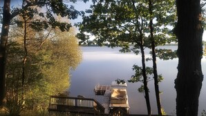 A dock extending into a calm lake, surrounded by trees and a wooden walkway.