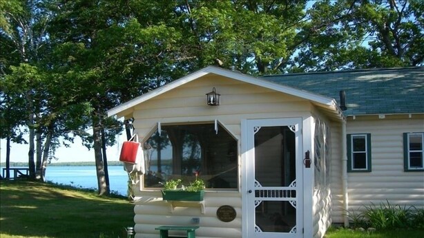 A small cabin with a porch, a bench, and a red mailbox.