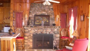 A cozy cabin interior with a stone fireplace, wooden walls, and a red armchair.