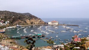 Un port de plaisance situé sur la côte, où de nombreux bateaux sont amarrés, un bâtiment imposant avec un toit rouge et un paysage vallonné en arrière-plan.