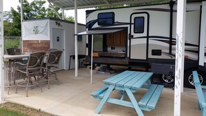 Parque para vehículos recreativos con techo, zona de comedor, mesa de picnic y asientos al aire libre.