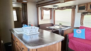 Cocina compacta de autocaravana con lavamanos, una mesita pequeña y un sofá con un cojín con diseño de dona.