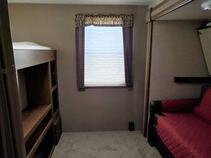A bedroom with a bunk bed, a window with curtains, and a wooden shelf unit.