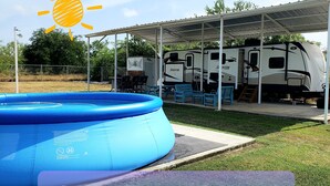 Un parque para vehículos recreativos con una piscina inflable azul y un área de picnic techada.
