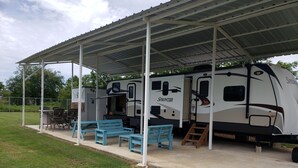 Parque para vehículos recreativos con techo, una caravana Sprinter, zona de estar al aire libre y una mesa de picnic.