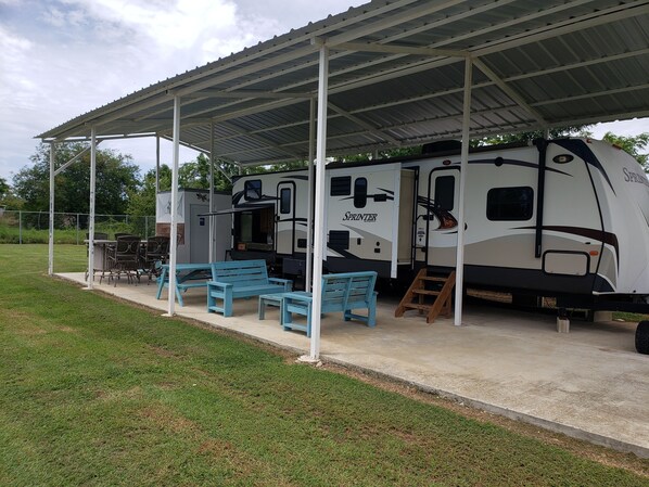 A covered RV park with a Sprinter RV, outdoor seating, and a picnic table.