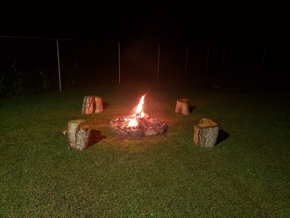 A fire pit with logs and stones in a grassy outdoor area at night. - El Camper, carretera hacia Combate, Cabo Rojo (Cabo Rojo)