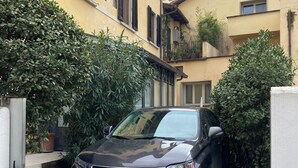 Un SUV Lexus negro estacionado en un camino de entrada estrecho entre dos edificios con paredes amarillas y contraventanas negras.