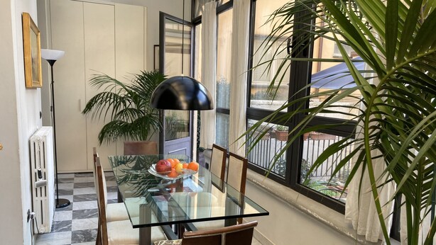 Un comedor con una mesa de vidrio, sillas y un frutero.