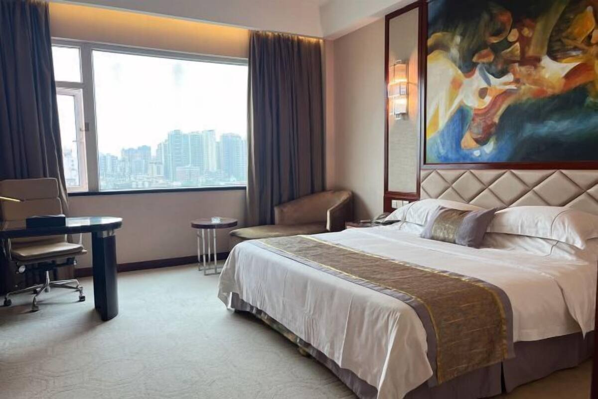 Een hotelkamer met een groot bed, een bureau, een stoel en uitzicht op de stadsgezichten door het raam.