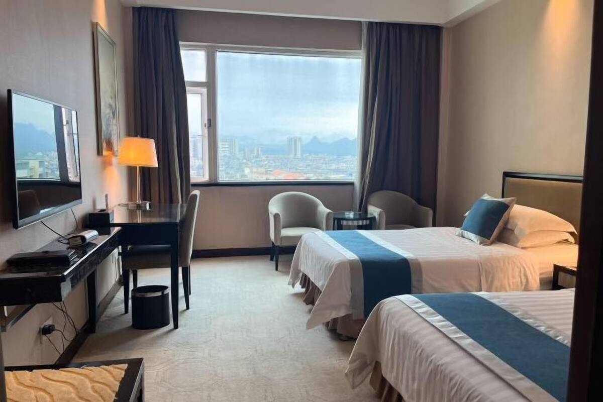 Hotelkamer met twee bedden, een bureau, een stoel, een televisie en een raam met uitzicht op de stad.