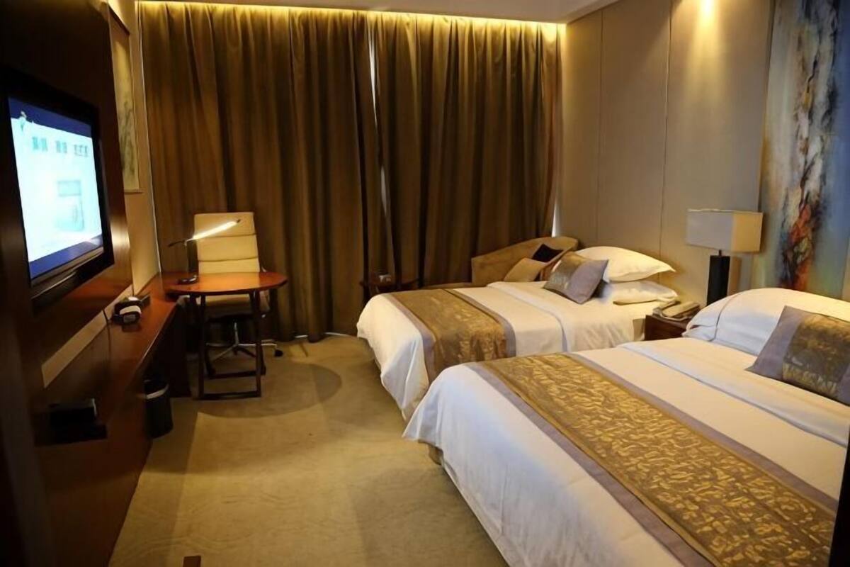 Een hotelkamer met twee bedden, een bureau met stoel, een televisie en een schilderij aan de muur.