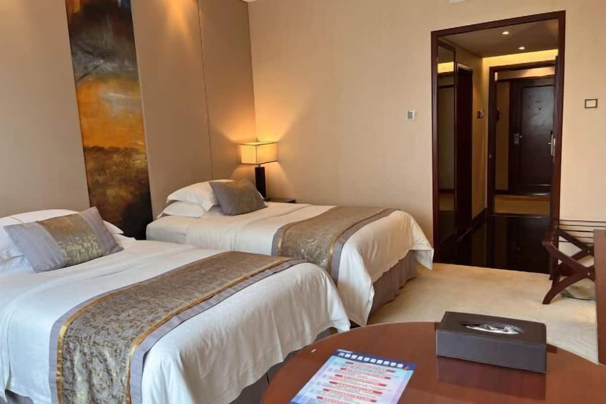 Een hotelkamer met twee bedden, een nachtkastje, een lamp, een tafel met een menukaart, en een deur naar een andere kamer.