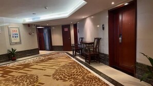 Eine Hotellobby mit Teppichmuster, Holztüren und einer Sitzecke mit Stühlen.