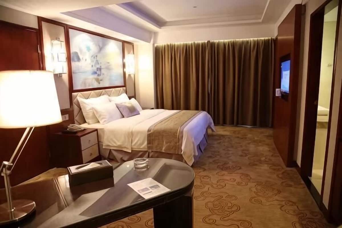 Een hotelkamer met een bed, nachtkastje, lamp en een televisie.