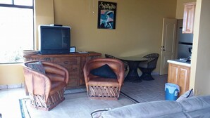 A living room with a television, two leather chairs, a sofa, a small table, and a poster on the wall. - Beachfront Studio Wonderful  Ocean Views, private access to beach (San Antonio del Mar)