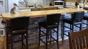 Een keuken met houten kastjes, een centraal eiland met barstoelen, een koelkast, een magnetron en een fornuis.