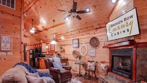 A cozy cabin interior with a fireplace, leather sofa, and a sign reading "BROKEN BOW Luxury CABINS".